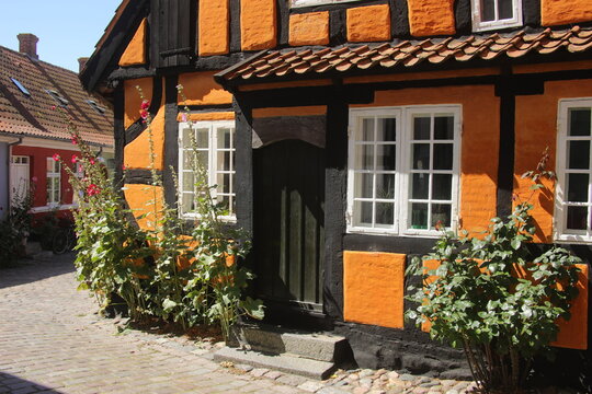 Facciata di una casa tradizionale con struttura a graticcio color arancione e nero, finestre bianche e fiori