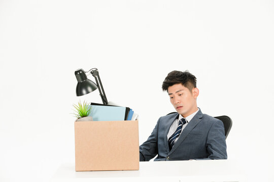 Sad businessman with personal belongings box after layoff at office desk