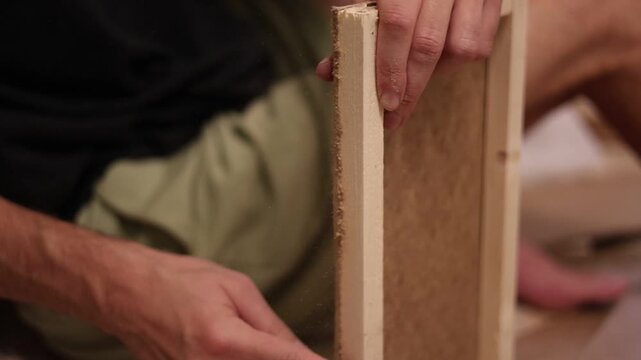 Craftsman sanding a wooden frame with sandpaper for smooth surface finishing during carpentry work