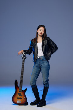 Young woman posing with electric bass guitar in studio