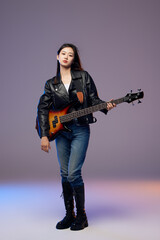 Fototapeta premium Young woman holding bass guitar in leather jacket studio portrait