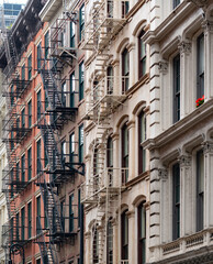 Obraz premium Historic brick facades of classic buildings with exterior iron fire escapes located in the iconic SoHo neighborhood in Manhattan, New York, displaying traditional urban architecture.