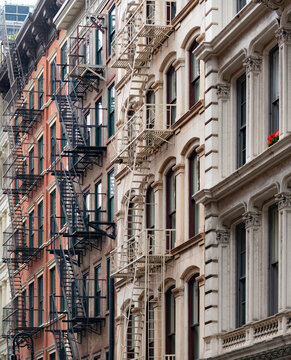 Historic brick facades of classic buildings with exterior iron fire escapes located in the iconic SoHo neighborhood in Manhattan, New York, displaying traditional urban architecture.