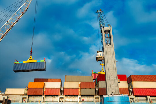 Heavy industrial cranes loading colorful shipping containers on a large cargo ship during global maritime freight transport operations at a busy commercial port.