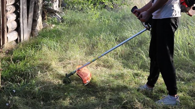 Gardener trimming weeds and overgrown grass with a motor scythe during summer dacha work