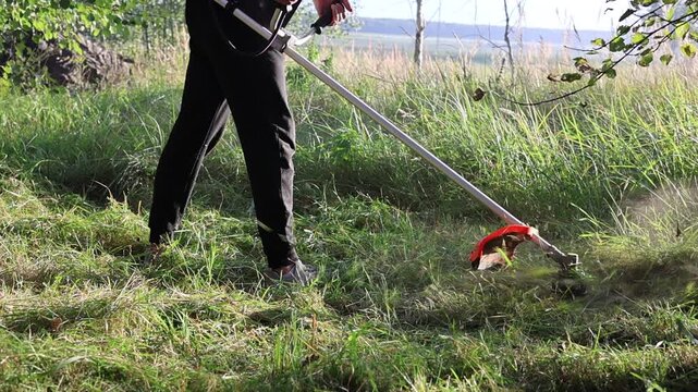 Gardener trimming weeds and overgrown grass with a motor scythe during summer dacha work