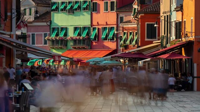 Burano Venice colorful street time lapse of blurred crowds walking past outdoor cafe terraces and vivid facade architecture in warm sunlight