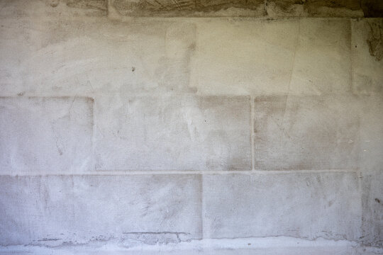Exterior block wall covered with adhesive mortar and reinforcing mesh, prepared for primer and final facade plaster during house construction and renovation.