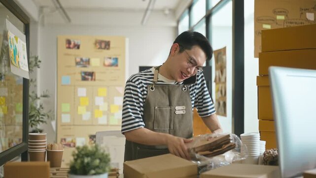 Asian male entrepreneur shirt talking on a smartphone with a customer to check order and stock details.
