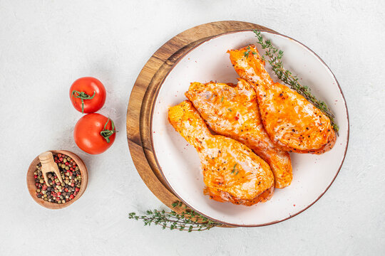 Grilled chicken thighs seasoned with spices on a white plate, garnished with fresh thyme, accompanied by cherry tomatoes and a bowl of mixed peppercorns on a wooden cutting board