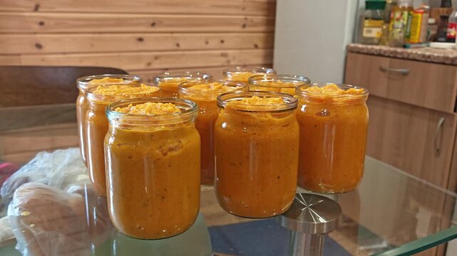 Rows of glass jars filled with orange squash caviar stored on a shelf at home, homemade preserves, canning season, rustic storage.