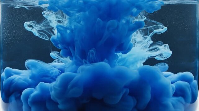 Cerulean blue ink swirling inside a glass cylinder filled with water creating an ethereal cloud formation