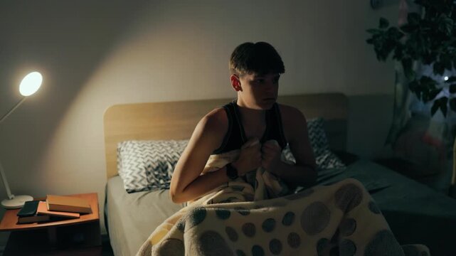 Front view of a scared teenager waking up suddenly in the dark bedroom.