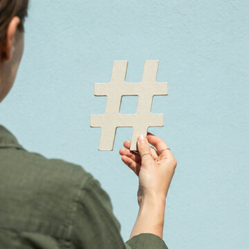 Person seen from behind holding a wooden hash symbol outdoors in soft daylight