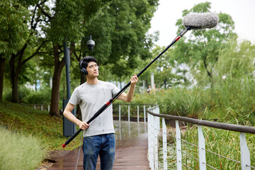 Man Recording Audio with Boom Microphone Outdoors in a Park © HaXuanDieu