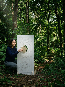 Woman placing a wooden jigsaw piece into a large puzzle in a forest in daylight