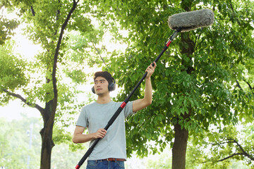 Man recording ambient sound with boom microphone in a park © HaXuanDieu