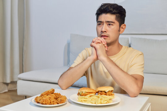 Thoughtful young man looking at unhealthy fast food meal at home