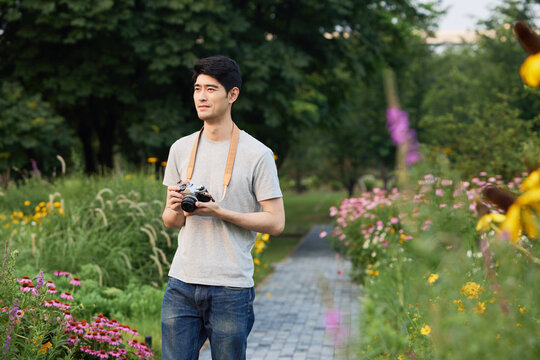 Young man holding a camera while standing in a flower garden park
