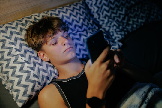 High angle of a teenage boy using his smartphone in the dark bedroom.