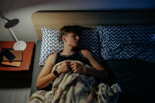 High angle of a sleeping teenage boy resting in the dark bedroom at night.