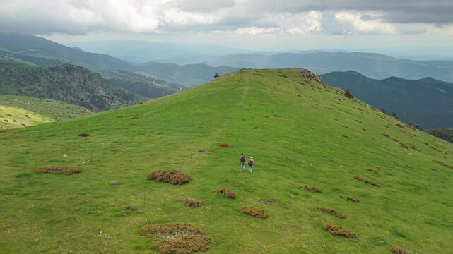 Two Hikers Crossing a Sunlit Green Ridge in the Pyrenees