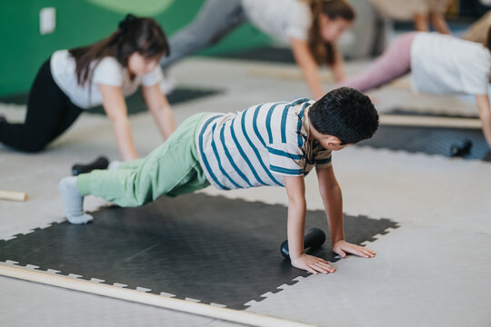 A group of kids hold plank positions on foam mats during a supervised fitness session. Children exercise together in a classroom-style workout focusing on core strength and balance.