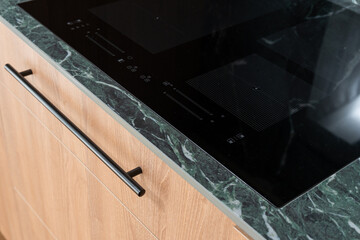 Induction hob on countertop in modern kitchen with wooden cabinets