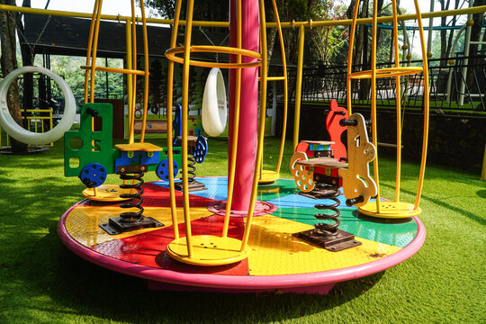 Colorful playground equipment with springs, swings, and climbing structures set on artificial grass under bright sunlight for children's outdoor fun and active play.