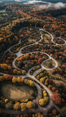 Fototapeta premium Aerial view of a winding road through a dense autumn forest with colorful trees and a misty background
