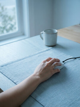 Hand using a white computer mouse on a blue grey pad by a bright window