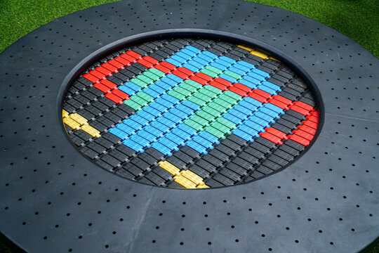 Colorful modular trampoline with red blue green yellow panels arranged in a circular pattern on a black perforated frame set on grassy surface, elegantly showcasing transportation.