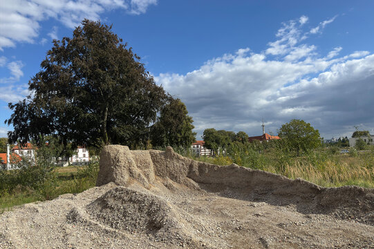 A construction site is shown with a large mound of gravel and a tree