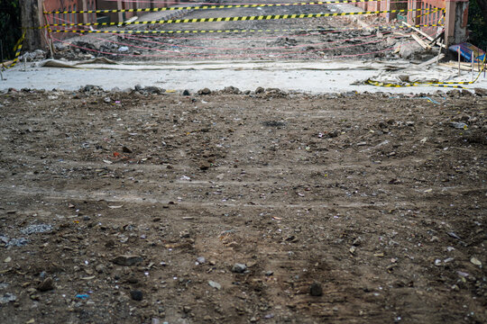 Dirt-covered construction site with scattered debris and yellow caution tape marking an unfinished area near brick walls and concrete structures, elegantly showcasing industrial.