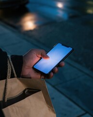 Fototapeta na wymiar Black friday sale mobile shopping with a man's hand holding a glowing blank phone screen over wet asphalt, mockup for app marketing
