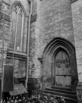 Black and white photo of a fragment of an old brick building facade with a vintage arched wooden door and a Gothic window