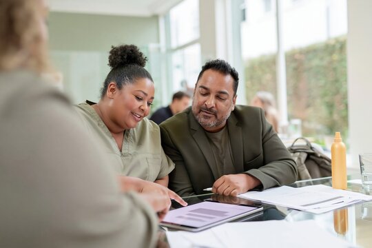 Travel health adviser in moss green scrubs pointing at a blank tablet mockup on a reflective glass table for medical consultation, copy space