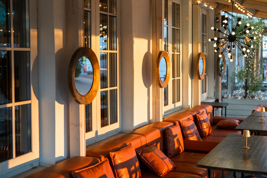 Interior of restaurant outdoor terrace with comfortable sofas and tables for overlooking sunset, street cafe open-air terrace with furniture and wooden framed mirrors hang on wall, comfy patio setting