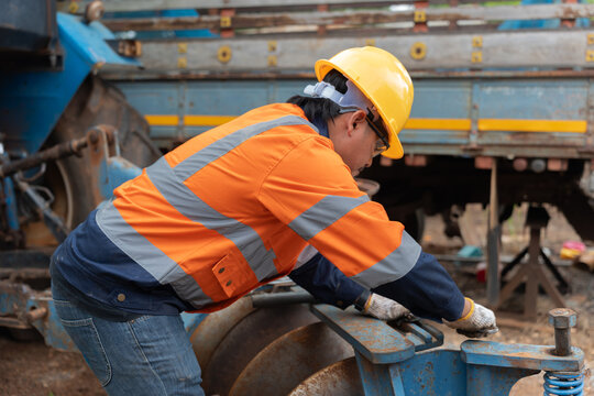 Agricultural mechanic inspects and maintains heavy farm equipment while wearing safety gear, checking a disc implement for preventive maintenance, reliable operation, and field productivity.