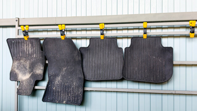 Car rubber mats hanging on a drying rack after washing, showcasing auto detailing service, vehicle maintenance, and interior cleaning process, preparing for reuse