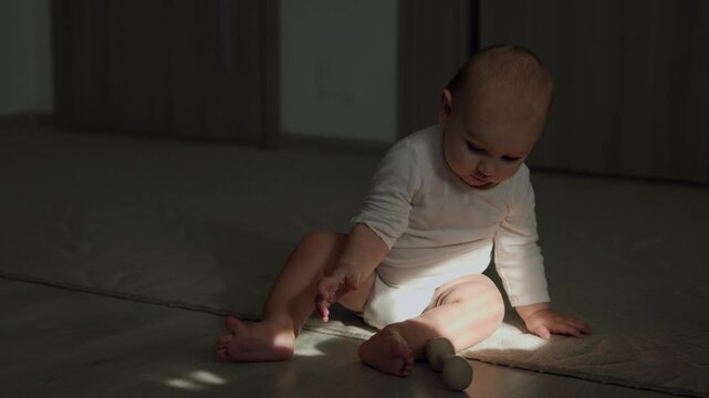 Infant in the teething phase crawling on an indoor floor and biting a silicone teether. Strong sunlight casts distinct shadows across the baby's face and body during daytime.