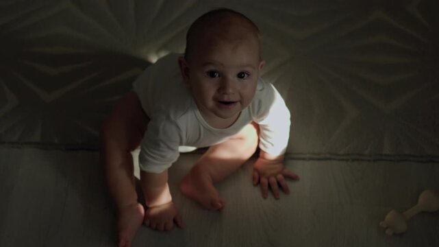 Infant in the teething phase crawling on an indoor floor and biting a silicone teether. Strong sunlight casts distinct shadows across the baby's face and body during daytime.