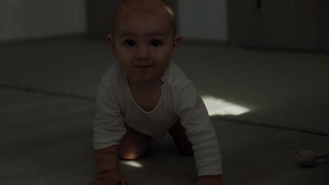 Infant in the teething phase crawling on an indoor floor and biting a silicone teether. Strong sunlight casts distinct shadows across the baby's face and body during daytime.