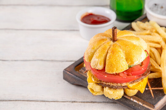 Pumpkin shaped burger. Tasty cheeseburger for Thanksgiving or Halloween party, made with pumpkin shaped bread bun, meat cutlets, melted cheese and fresh vegetables, with ketchup sauce, french fries