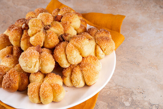 Pumpkin spice buns with almond nuts, cinnamon and sugar crunch. Autumn baking idea, pumpkin puree based vegetable rolls in form of small pumpkins. Tiny sweet pumpkin shaped buns on white plate,
