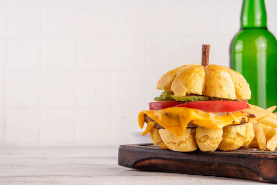 Pumpkin shaped burger. Tasty cheeseburger for Thanksgiving or Halloween party, made with pumpkin shaped bread bun, meat cutlets, melted cheese and fresh vegetables, with ketchup sauce, french fries