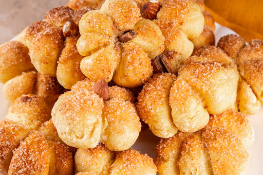 Pumpkin spice buns with almond nuts, cinnamon and sugar crunch. Autumn baking idea, pumpkin puree based vegetable rolls in form of small pumpkins. Tiny sweet pumpkin shaped buns on white plate,