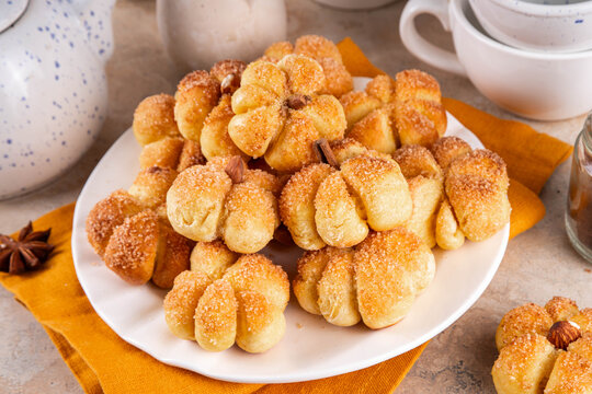 Pumpkin spice buns with almond nuts, cinnamon and sugar crunch. Autumn baking idea, pumpkin puree based vegetable rolls in form of small pumpkins. Tiny sweet pumpkin shaped buns on white plate,