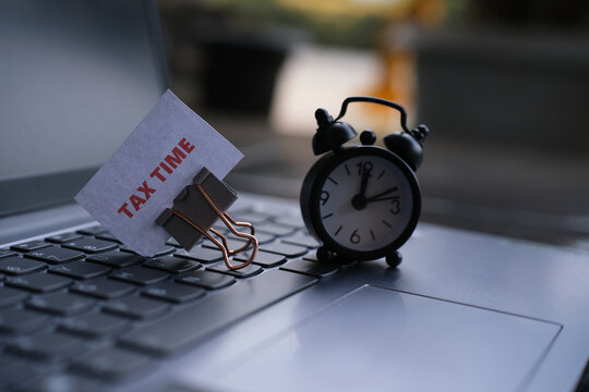 "TAX time" text and an alarm clock above a keyboard. Tax payment timing concept. A reminder to pay taxes on time.