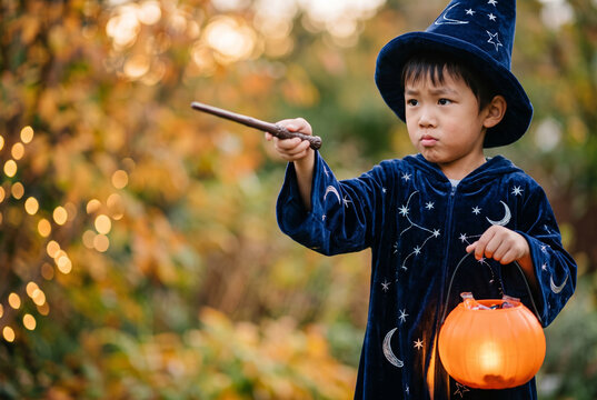 Young boy in wizard costume holding pumpkin lantern and wand  